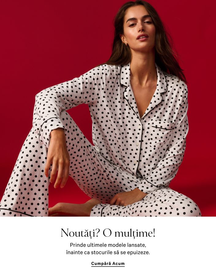 Femeie purtând un set de pijama alb, cu cămașă și pantaloni scurți, stând într-un cadru de ușă.